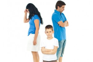 Upset boy standing with arms folded in front of parents with problems against white background